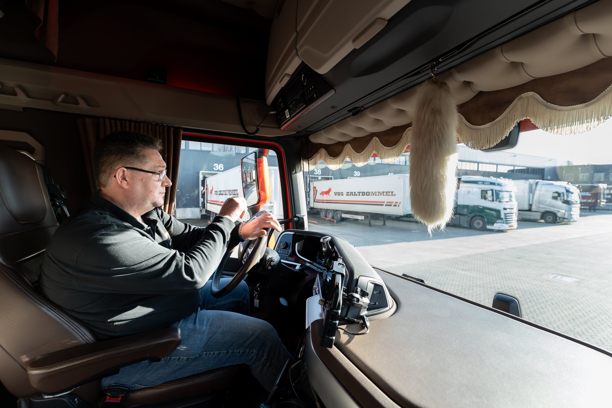 Chauffeur achter het stuur in truckercabine met Vos Zaltbommel trailers op het erf