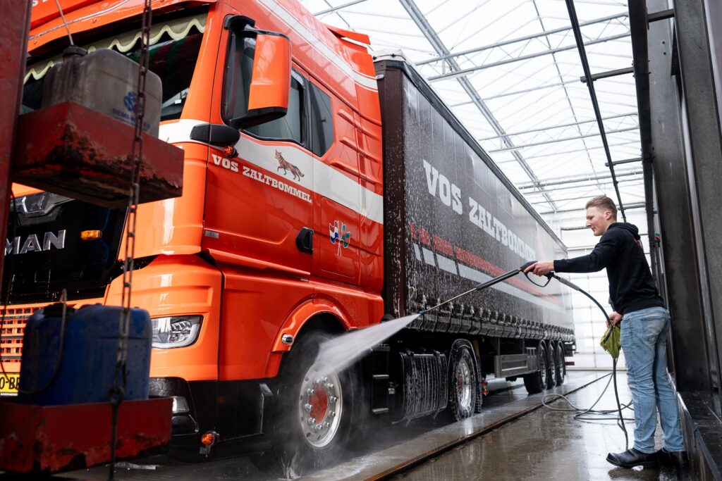 Medewerker wast vrachtwagen met trailer met waterslang bij Vos Transport