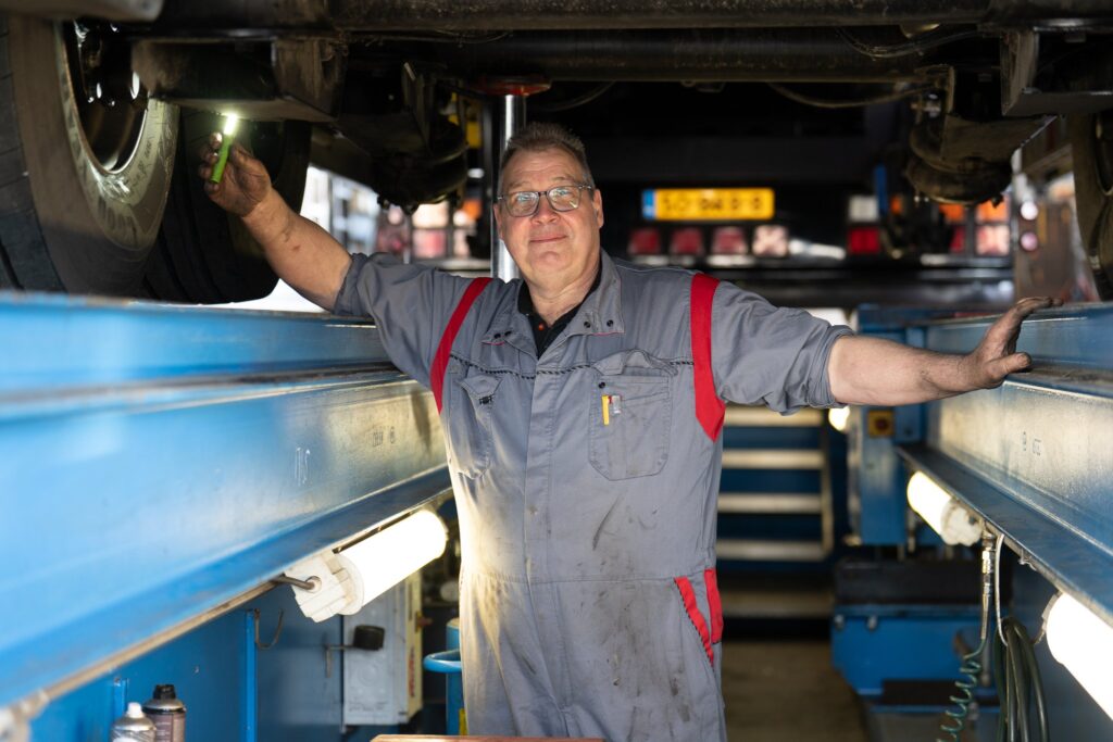 Vos Transport monteur poseert glimlachend onder truck op de hefbrug