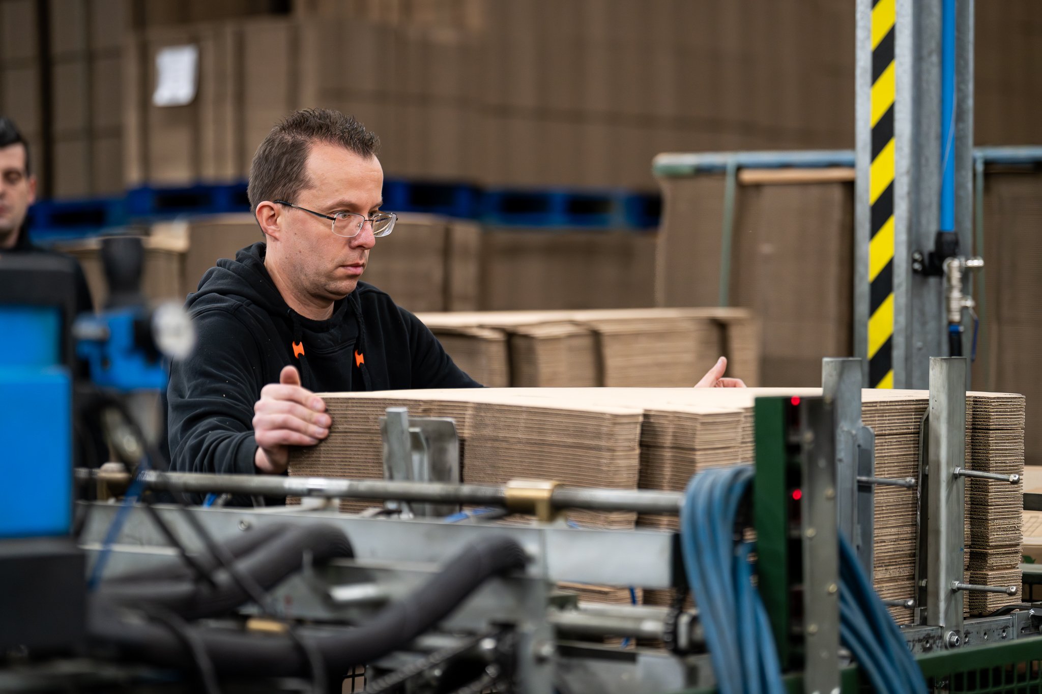 Medewerker voert karton in bij de verpakkingslijn in de Vos Transport assemblagehal